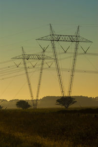 Low angle view of electricity pylon against sky during sunset