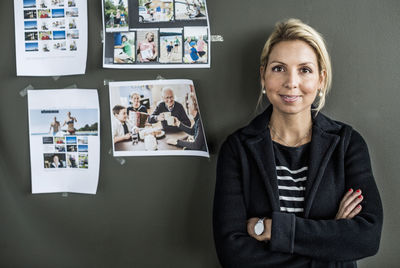 Portrait of mid adult businesswoman standing arms crossed against wall in office
