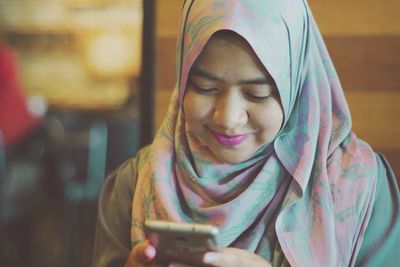 Close-up of smiling young woman in hijab using mobile phone