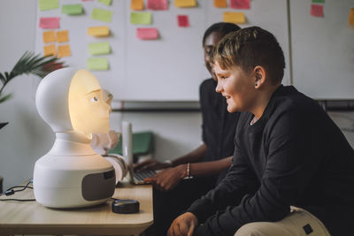 Smiling boy communicating with illuminated ai robot in innovation lab