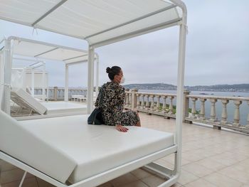 Full length of woman sitting on railing against sea