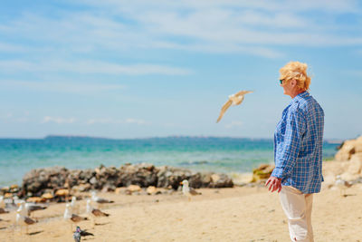 Elderly woman standing on the beach and looking into the distance