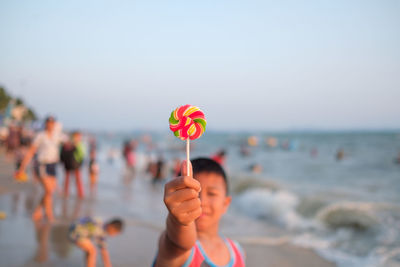 Boy holding lollipop at beach against sky