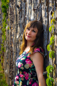 Portrait of woman standing by tree trunk in forest