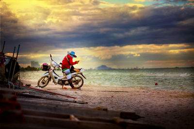 Man riding bicycle on road against cloudy sky
