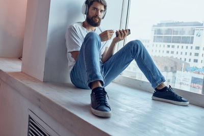 Full length of young man looking away while sitting on window