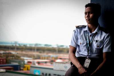 Thoughtful man in uniform sitting against clear sky