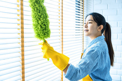 Side view of woman cleaning window at home