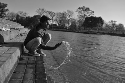 Side view of boy splashing water while crouching by river