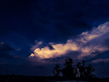 Low angle view of silhouette trees against dramatic sky