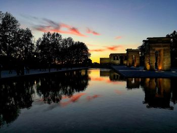 Reflection of silhouette trees in water against sky during sunset