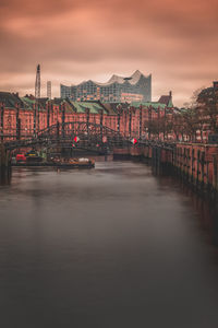 Bridge over river amidst buildings in city at sunset