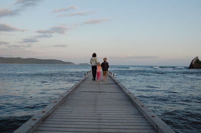 Rear view of people on sea against sky during sunset