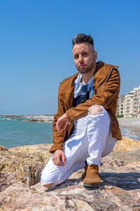 Man sitting by sea against clear sky