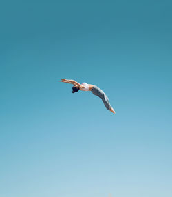 Full body side view of faceless female acrobat performing somersault high in air against clear cloudless blue sky on summer day