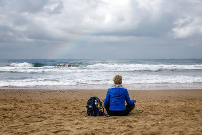 Rear view of woman sitting on beach against sky