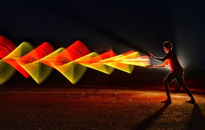 Side view of young man with illuminated light painting standing against sky at night