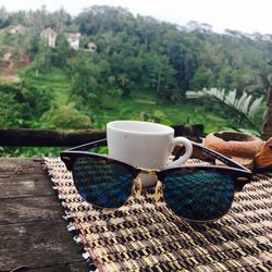 Close-up of cup with sunglasses on table against field