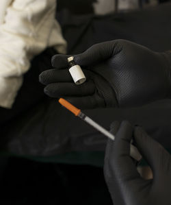 Glass bottle with injection shot, hands in black gloves holding syringe with needle, ampoule with