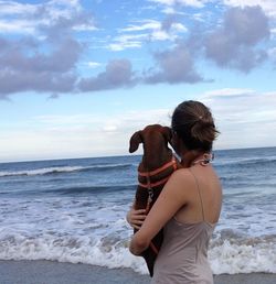 Rear view of friends standing on beach against sky