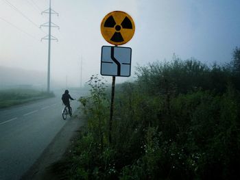 Boy riding bicycle on road against sky