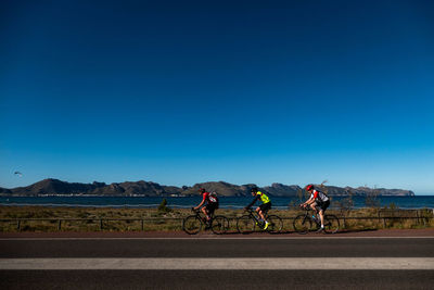 People riding bicycle on road against clear blue sky