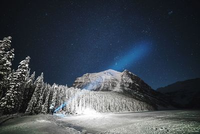 Distant view of person showing flashlight by snowcapped mountain against star field at night