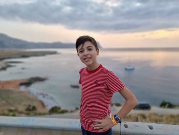 Portrait of happy boy standing in water against sky