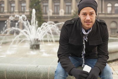 Portrait of young man sitting on fountain