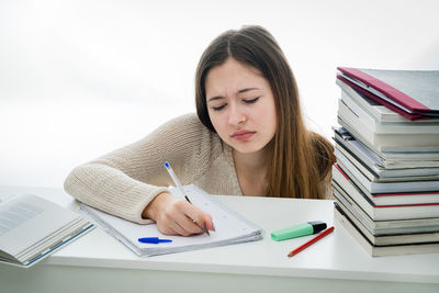 Worried teenage girl writing on book against white background