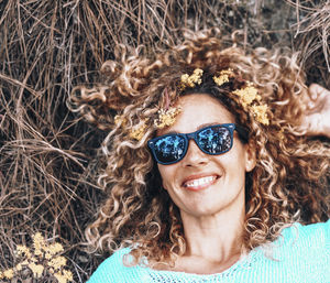 Portrait of smiling young woman wearing sunglasses standing against plants