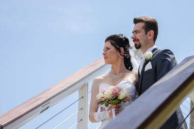 Low angle view of bride and bridegroom looking away while standing amidst railings