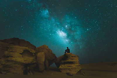 Man sitting on rock against star field