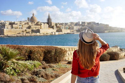 Woman with hat goes down along malta waterfront looking stunning panoramic view of valletta, malta