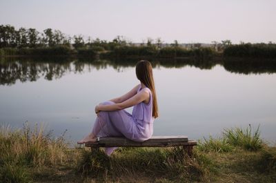 Rear view of woman sitting by lake against sky