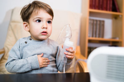 Cute boy looking away while holding oxygen mask at home