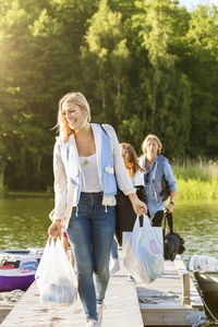 Happy friends with luggage walking on pier at lake