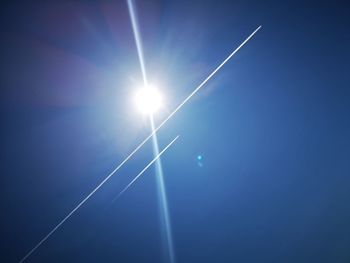 Low angle view of vapor trail against blue sky on sunny day