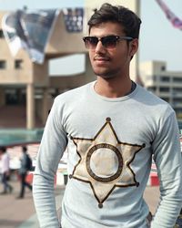 Young man wearing sunglasses while standing against building