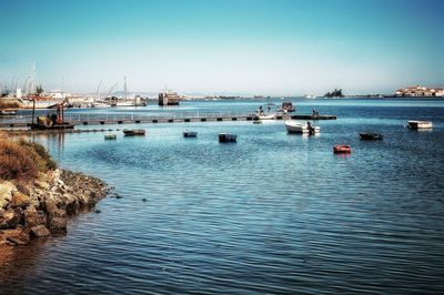 Sailboats moored in sea against clear blue sky