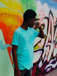 Full length of young man standing against graffiti wall