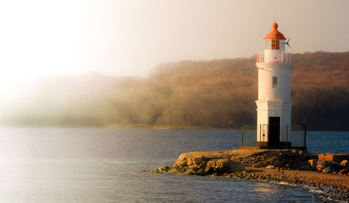 Lighthouse by sea against sky