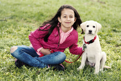 Girl with dog sitting on grassy field at park