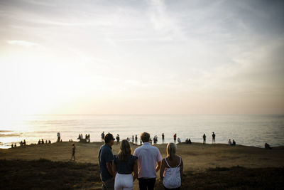 Family looking at sea while standing on cliff against sky during sunset