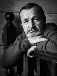 Portrait of senior man wearing sweater leaning on wooden railing while sitting at home