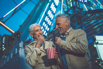 Smiling couple eating popcorn while standing at carnival