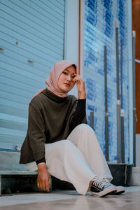 Full length of young woman in hijab sitting against wall