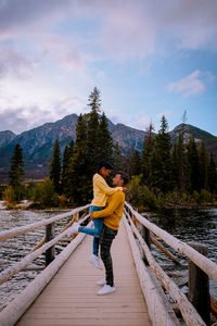 Couple standing on footbridge against sky