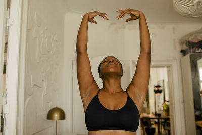 Woman exercising with eyes closed and arms raised at home