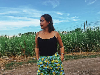 Young woman looking away while standing on land against sky